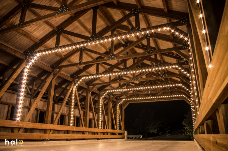 Warm lights illuminate a wooden bridge's intricate beams under a night sky