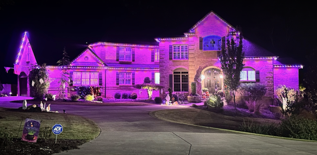 A brightly lit house glows with purple holiday lights against the night sky